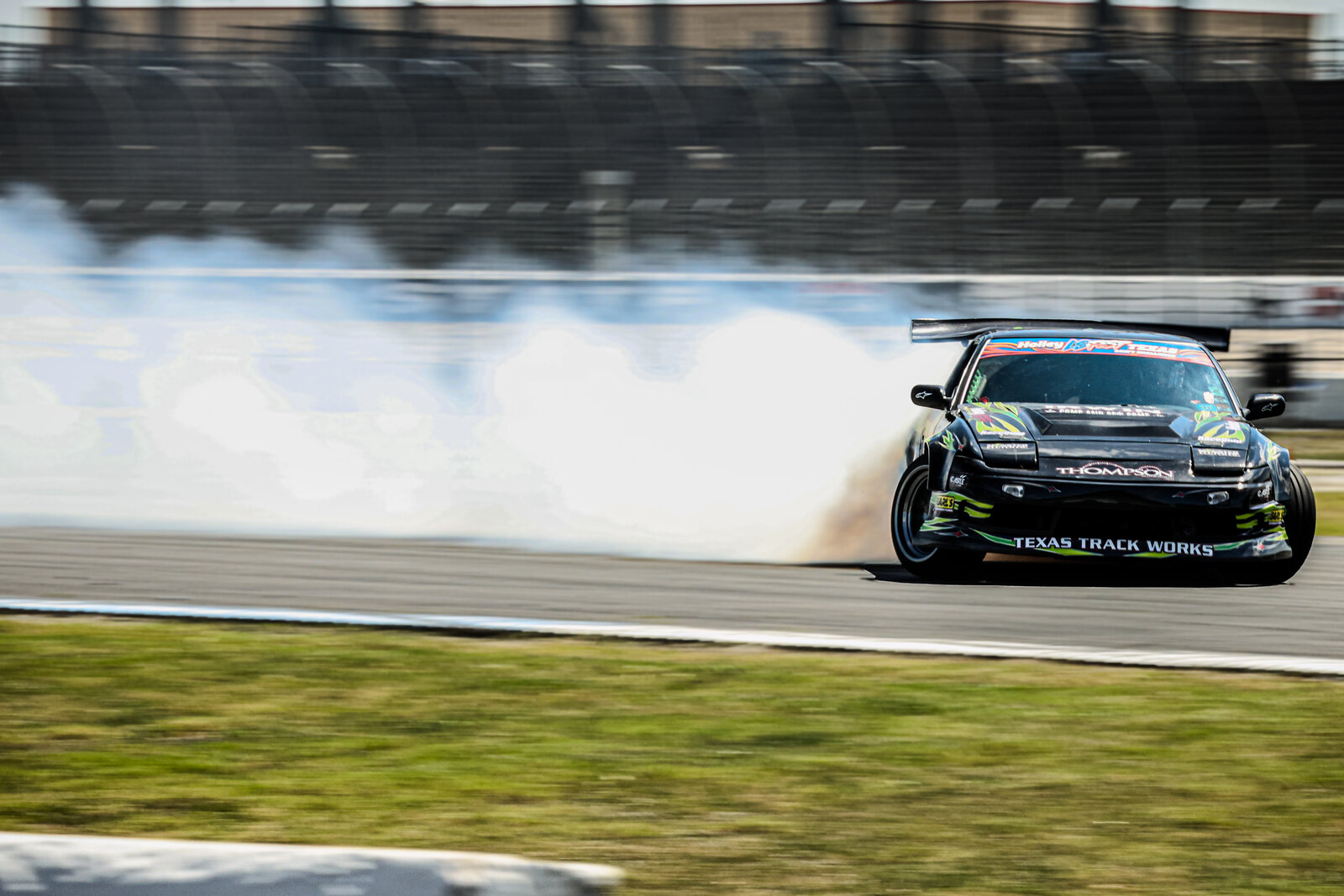 Drift car mid-corner at LS Fest Texas — black coupe at full lock with a long smoke trail behind it