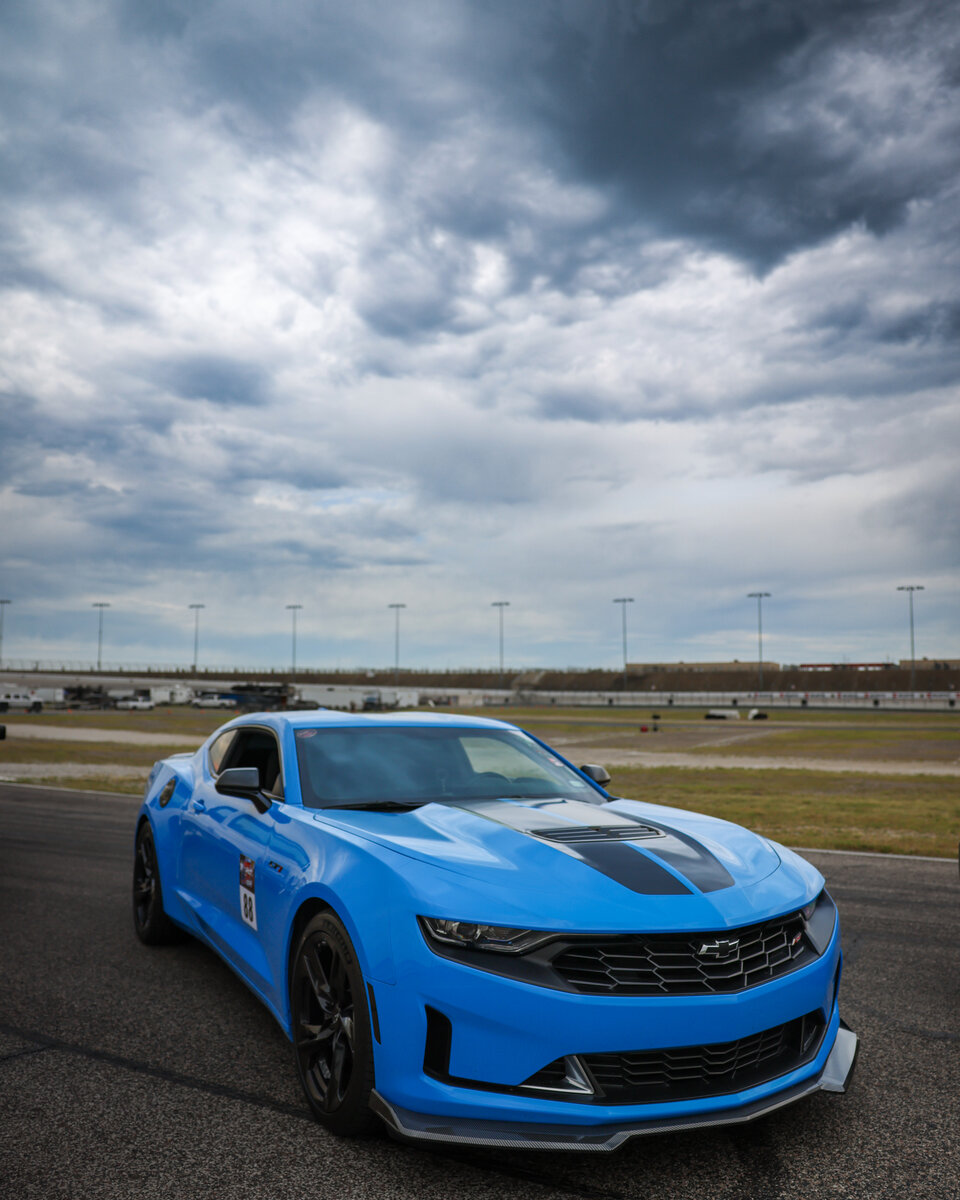 Blue modern Camaro staged on the track at LS Fest, dramatic overcast sky behind it
