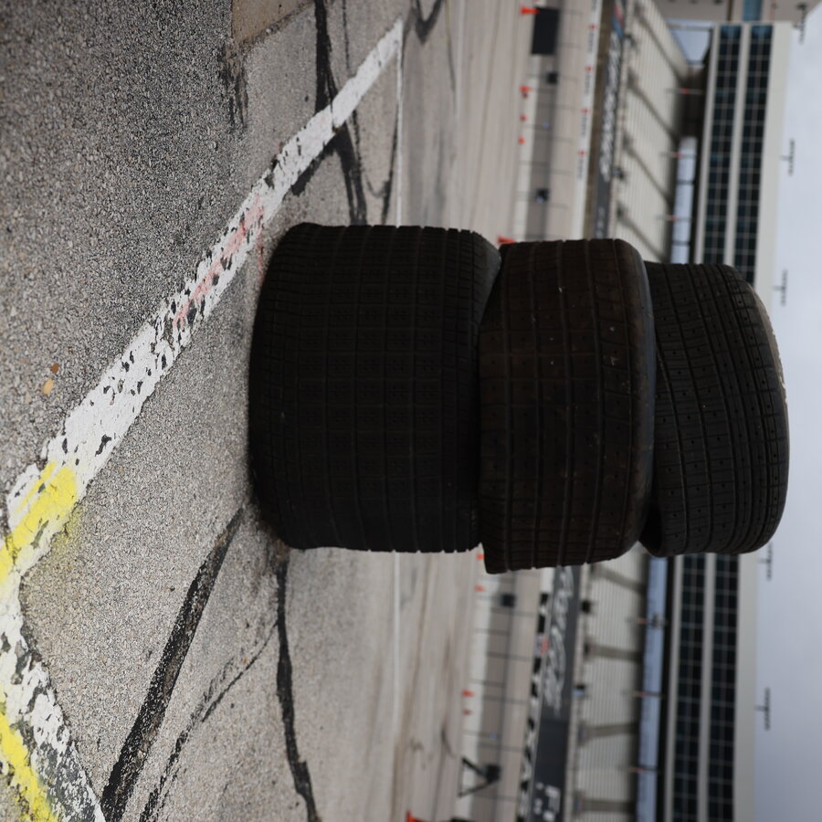 Three race tires stacked on the paddock surface, with track-grid striping visible