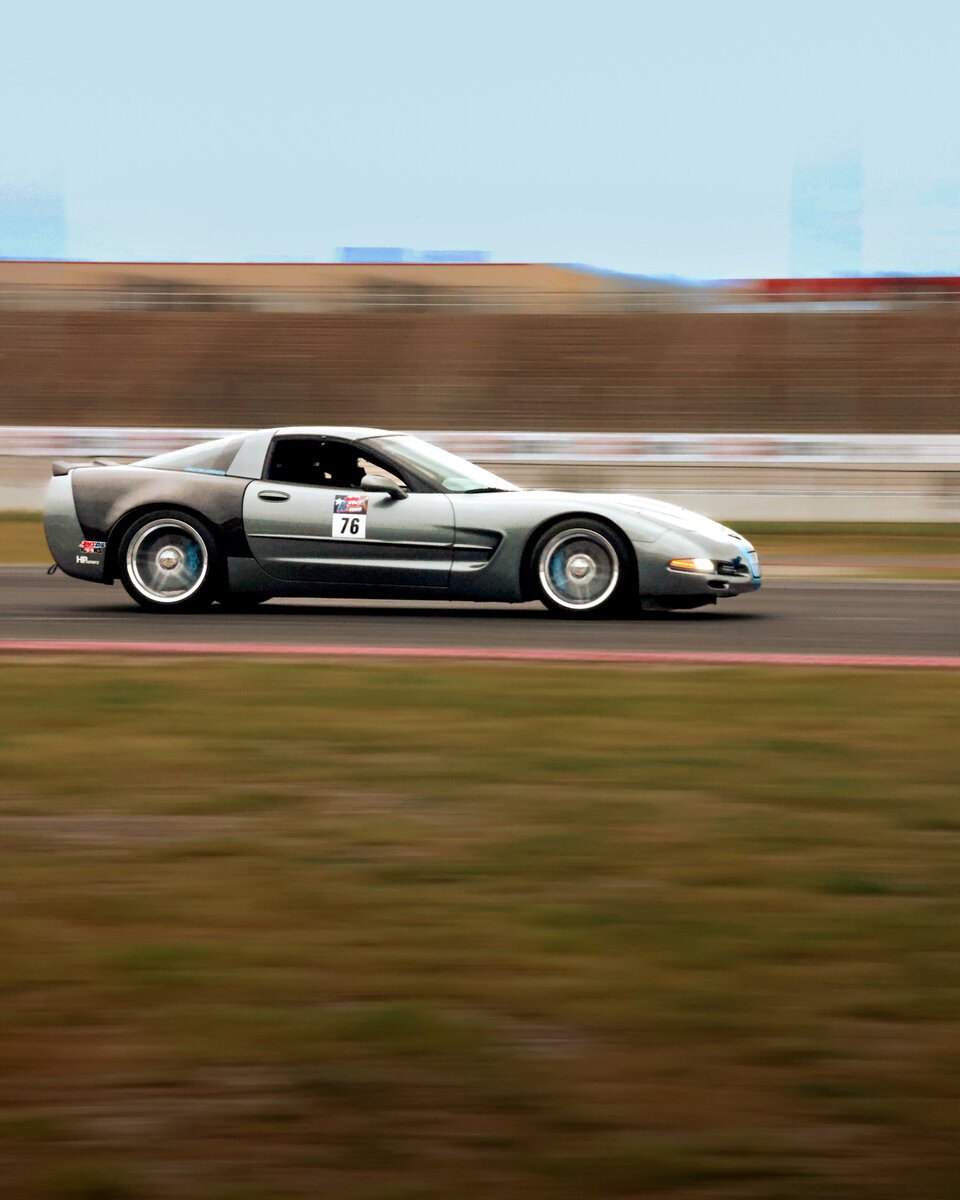 Silver C5 Corvette mid-corner captured in a pan blur — motion frozen with the background streaked