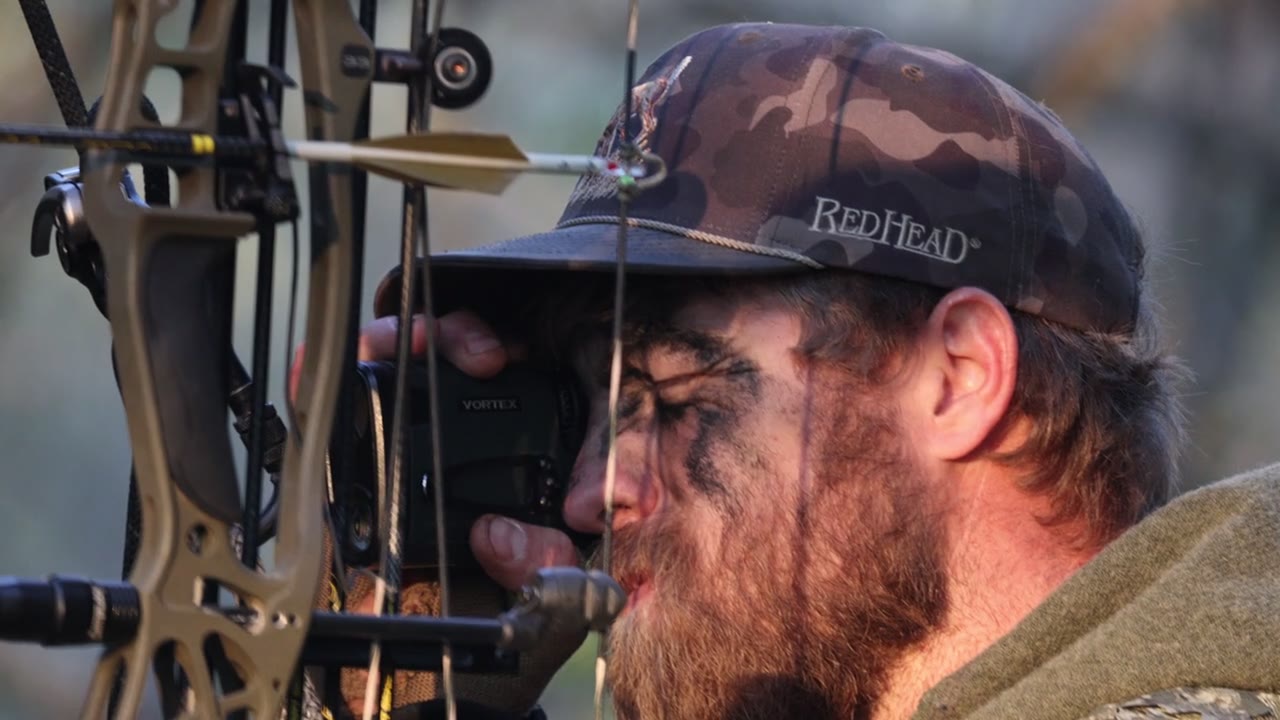 Bowhunter at full draw, camo face paint, Texas lease